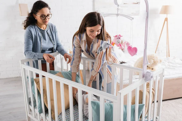 Feliz Madre Mirando Bebé Niño Cuna Cerca Africano Americano Amigo — Foto de Stock