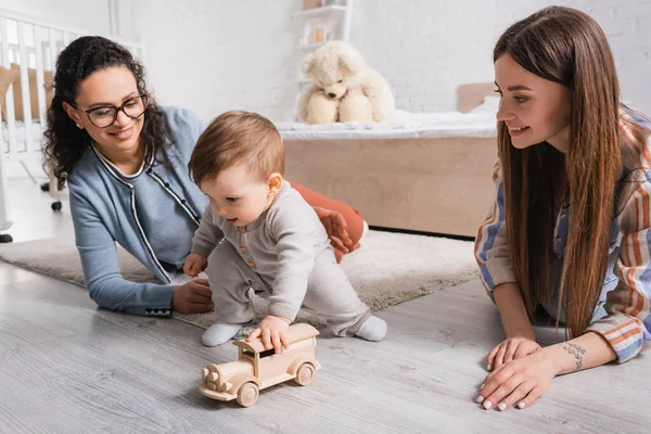 Säugling Spielt Mit Holzspielzeugauto Der Nähe Glücklicher Multiethnischer Frauen — Stockfoto