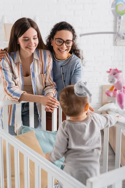 Heureux Interracial Femmes Regardant Flou Bébé Garçon Dans Bébé Lit — Photo