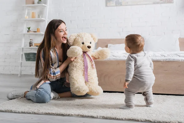 Erstaunte Junge Mutter Hält Teddybär Der Nähe Ihres Kleinen Sohnes — Stockfoto