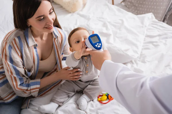 Pediatra Examinando Menino Com Termômetro Sem Contato Perto Mãe Feliz — Fotografia de Stock