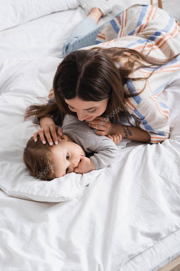 high angle view of tattooed mother looking at baby boy lying on bed