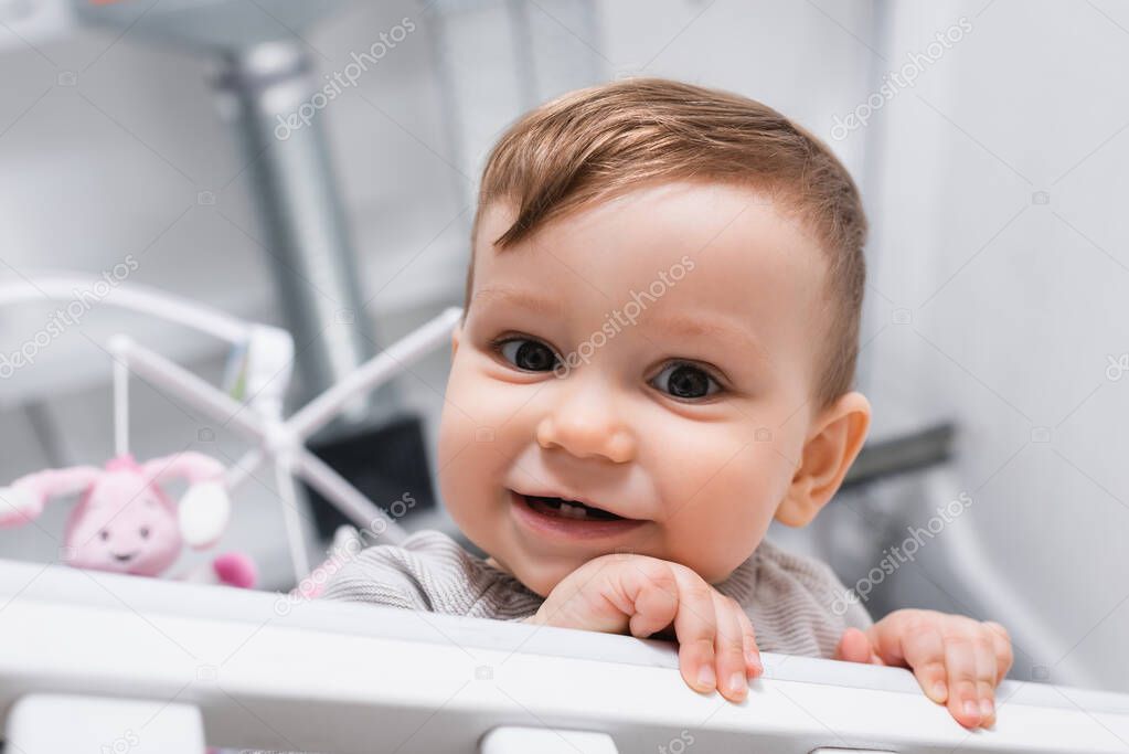 close up of smiling infant boy looking at camera from baby crib 