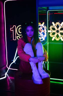young asian woman in bright clothing sitting on floor near neon sign