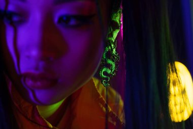 neon lighting on face of young blurred asian woman with dragon earring 