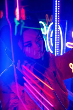 neon lighting near young asian woman talking on retro payphone outside 