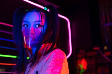 young asian woman in face shield near neon lighting 