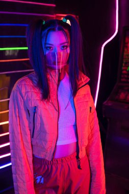 stylish young asian woman in face shield near neon lighting 