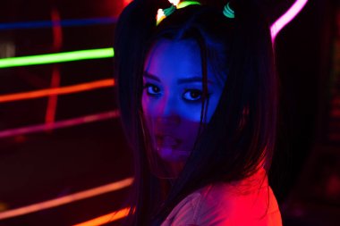 young asian woman in face protective shield near neon lighting 