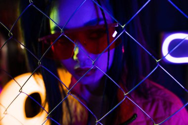 metallic fence near trendy young asian woman in sunglasses on blurred background 