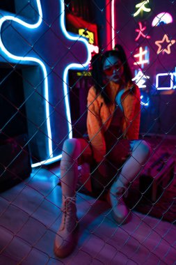 metallic fence near trendy young asian woman in sunglasses posing on blurred background 