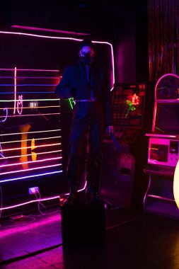 full length of neon lighting on young asian woman in gas mask with knife 