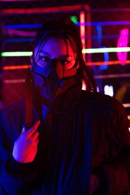 neon lighting on young asian woman in gas mask holding knife