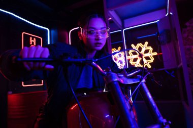 young asian woman in sunglasses riding motorcycle outside 