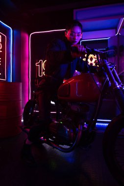 young asian woman in sunglasses riding motorcycle near neon sign 