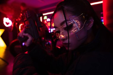 armed asian woman in sunglasses holding blurred gun outside  clipart