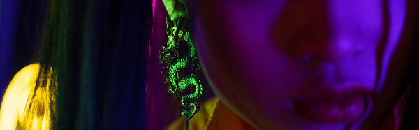 обрезанный вид молодой размытой женщины с драконьей сережкой, баннером