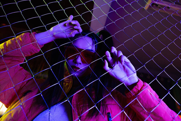 low angle view of trendy young asian woman in sunglasses near metallic fence 