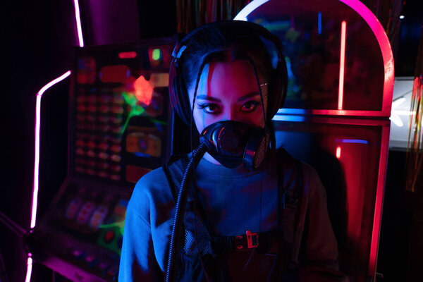 young asian woman in gas mask and wireless headphones looking at camera