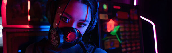 young asian woman in gas mask and wireless headphones looking at camera, banner