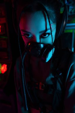 young asian woman with scar in gas mask and wireless headphones looking at camera clipart