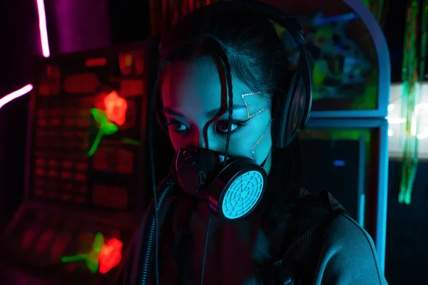 young asian woman with scar in gas mask and wireless headphones looking away