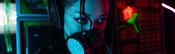 young asian woman with scar in gas mask and wireless headphones looking away, banner