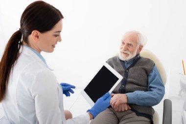 Diş hekimindeki kıdemli hasta elinde tabletle doktordan danışmanlık alıyor.