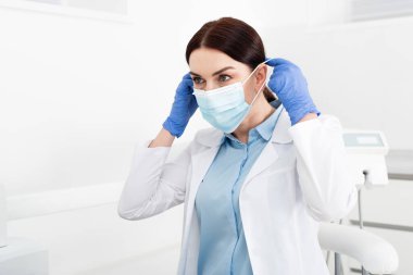 Diş kliniğinde tıbbi maske takan lateks eldivenli dişçi. 