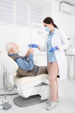 İlgili diş hekimi dişçi koltuğunda yatan yaşlı hastaya bir bardak su veriyor. 