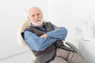 Klinikte dişçi koltuğunda çapraz kollu oturan son sınıf öğrencisi.