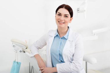 portrait of cheerful dentist in white coat sitting in dental clinic  clipart