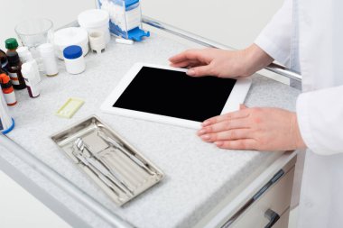 Kadın dişçi ellerinin tepside metal diş aletlerinin yanında boş ekranlı tablet kullanmasının kırpılmış görüntüsü