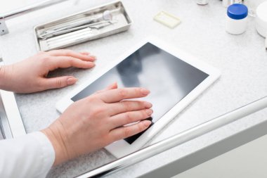 Tıbbi masadaki diş malzemelerinin yanında boş ekranla tablete yazı yazan kadınların kısmi ekin görüntüsü