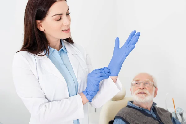 Dentista Bata Blanca Ajustando Guantes Látex Cerca Paciente Anciano Sentado — Foto de Stock