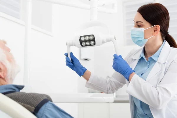 Zahnarzt Mit Medizinischer Maske Und Blauen Latexhandschuhen Berührt Medizinische Lampe — Stockfoto