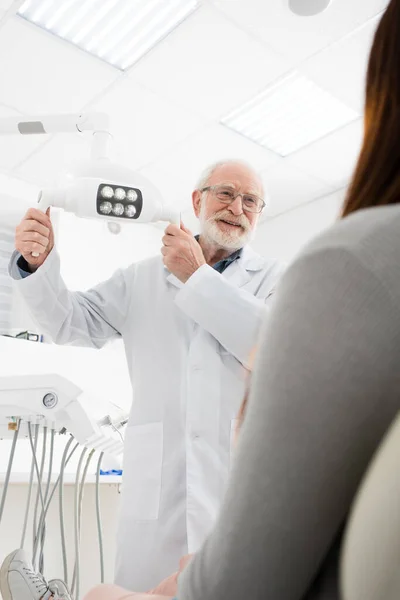 Веселий Старший Стоматолог Торкається Медичної Лампи Перед Жінкою Стоматологічному Кріслі — стокове фото