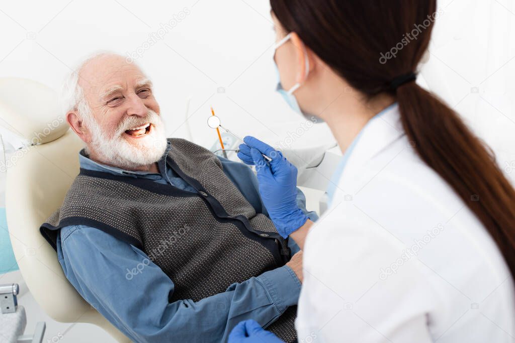 smiling senior man having teeth treatment by dentist in latex gloves in dental clinic