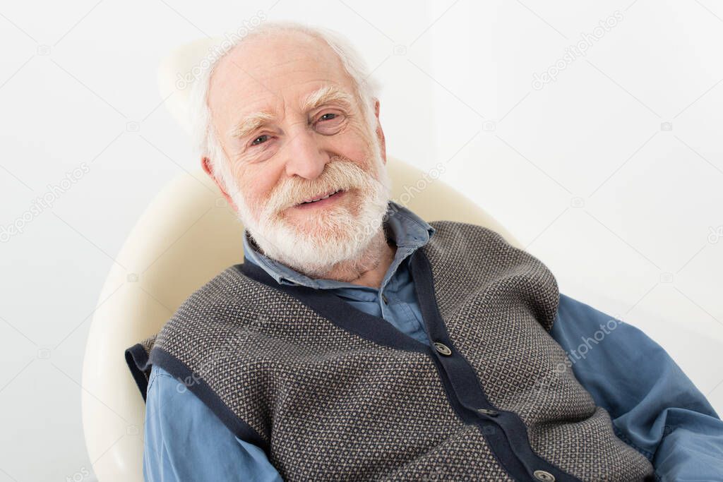 smiling senior man sitting in dental chair and looking at camera isolated on grey