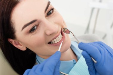 Doktor tarafından klinikte lateks eldivenli diş muayenesi yapılan mutlu yetişkin kadın görüntüsü. 