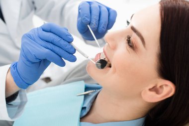 Yetişkin bir kadının klinikte lateks eldivenli bir doktor tarafından diş muayenesi yaptırması.