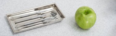 Tepside metal diş aletlerinin yüksek açılı görüntüsü ve tıbbi masada yeşil elma, afiş