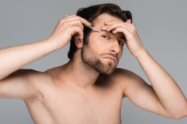 Genç sakallı ve gömleksiz bir adam. Cımbızlı kaşları gri renkte.