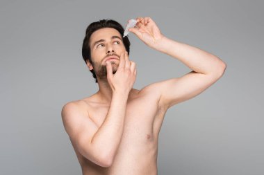 shirtless man applying eye drops isolated on grey clipart