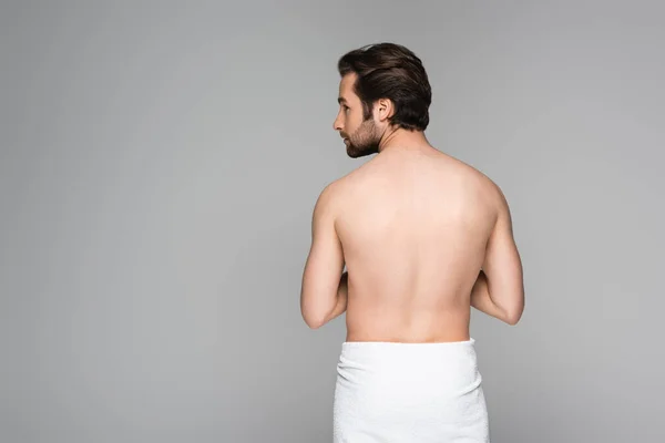 shirtless man wrapped in towel standing and looking away isolated on grey