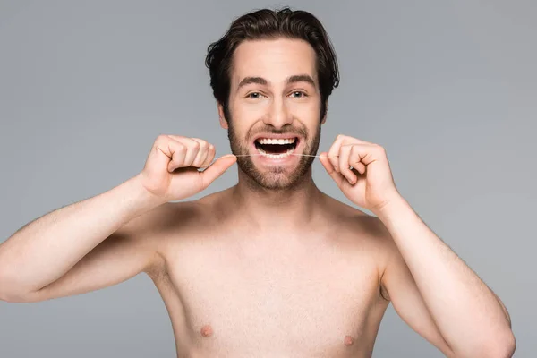 happy and shirtless man flossing teeth isolated on grey