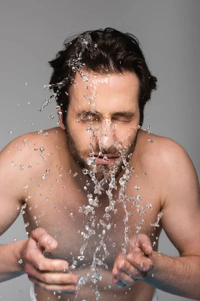 bearded man with closed eyes washing face isolated on grey