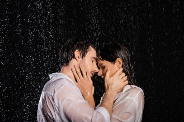 Kara arka planda yağmur damlalarında el ele tutuşan tutkulu romantik çift.