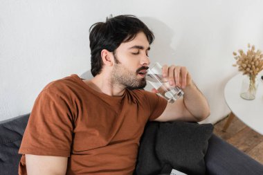 Sakallı adam sıcaktan acı çekerken su içiyor.