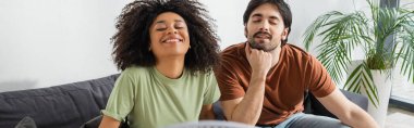 happy interracial couple sitting on couch in living room, banner clipart